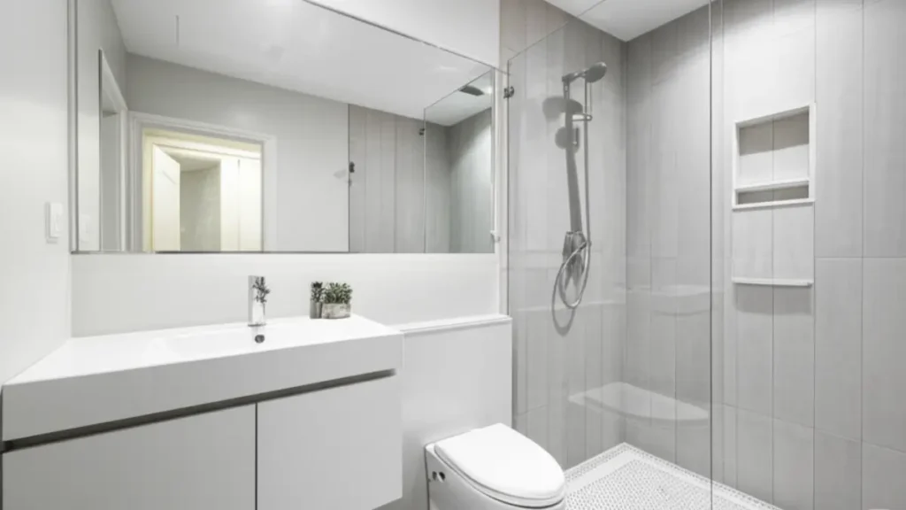 Imagem paisagem de um projeto de banheiro pequeno com foco em louças e metais modernos, incluindo um vaso sanitário compacto, pia elegante e box de vidro transparente que contribuem para a funcionalidade e o visual clean do ambiente.